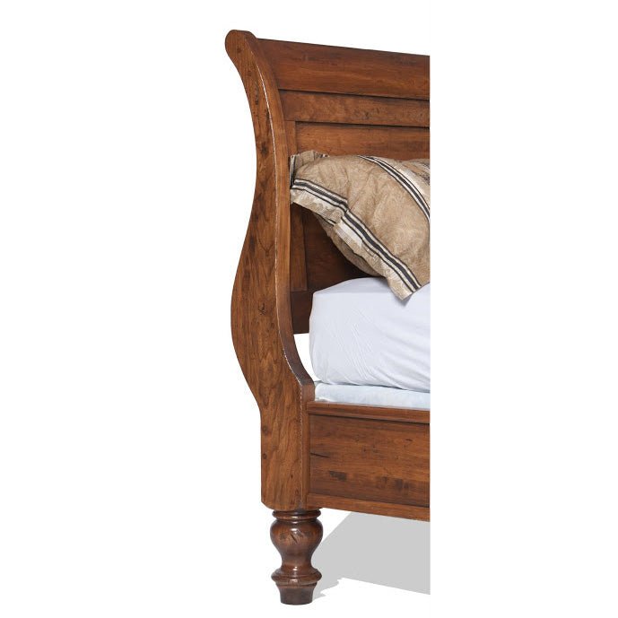 Close-up of the scrolled sleigh headboard curve in rustic cherry above a turned bun foot