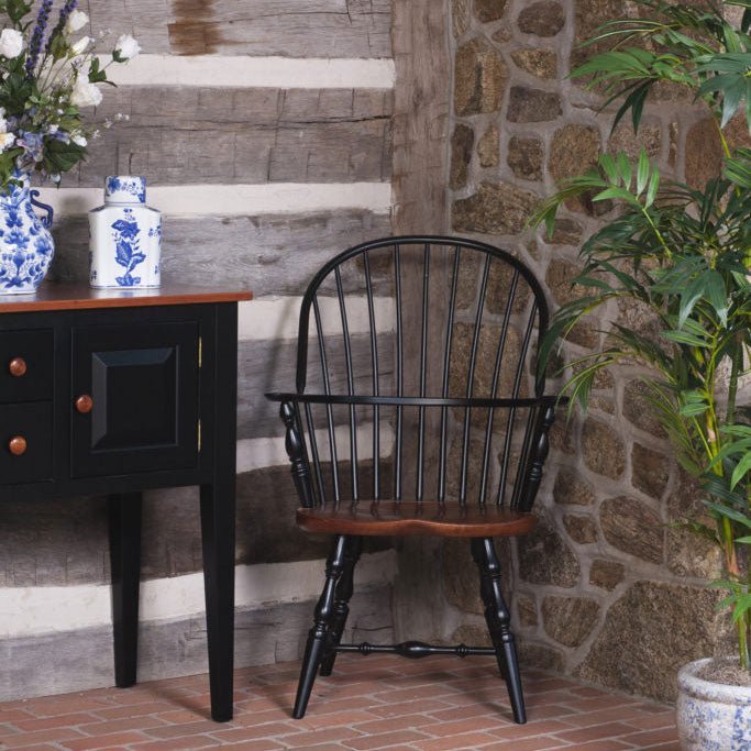 Black painted Windsor arm chair with natural wood saddle seat set beside a black hall table in a log and stone entry