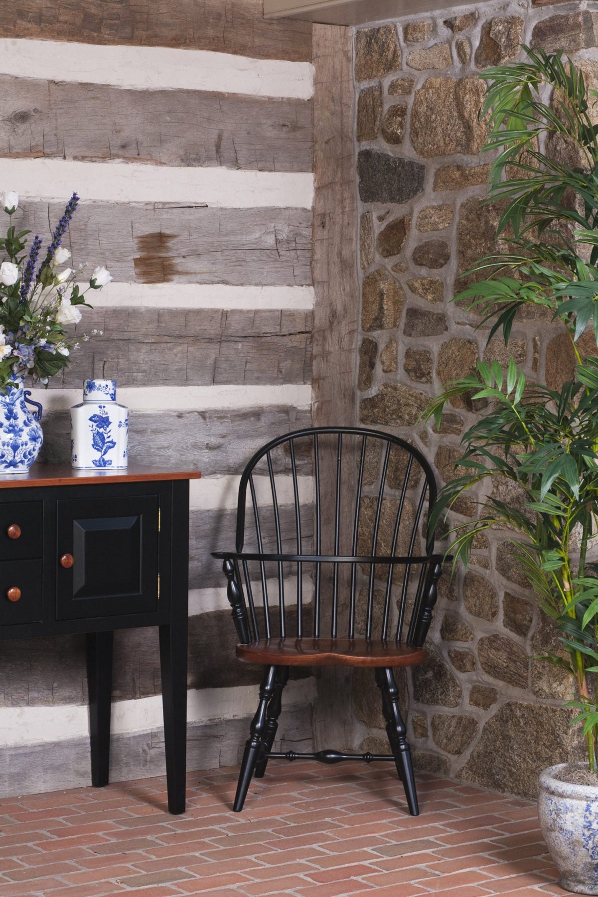 Two-tone black Windsor arm chair with stained saddle seat and spindle back staged against a whitewashed log cabin wall