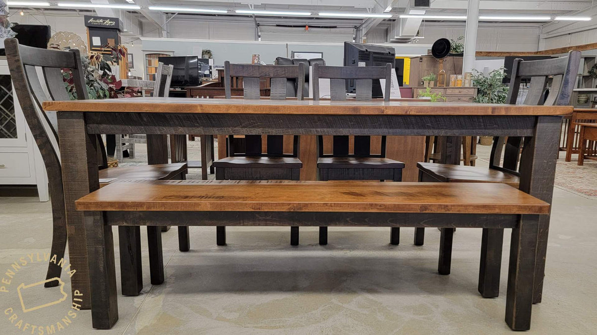 Rustic dining table and bench with warm stained plank tops and dark charcoal bases, chairs pulled in, shown in a showroom