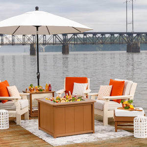 Cedar poly ice pit table brimming with bottles and citrus on a riverside dock under a cream patio umbrella