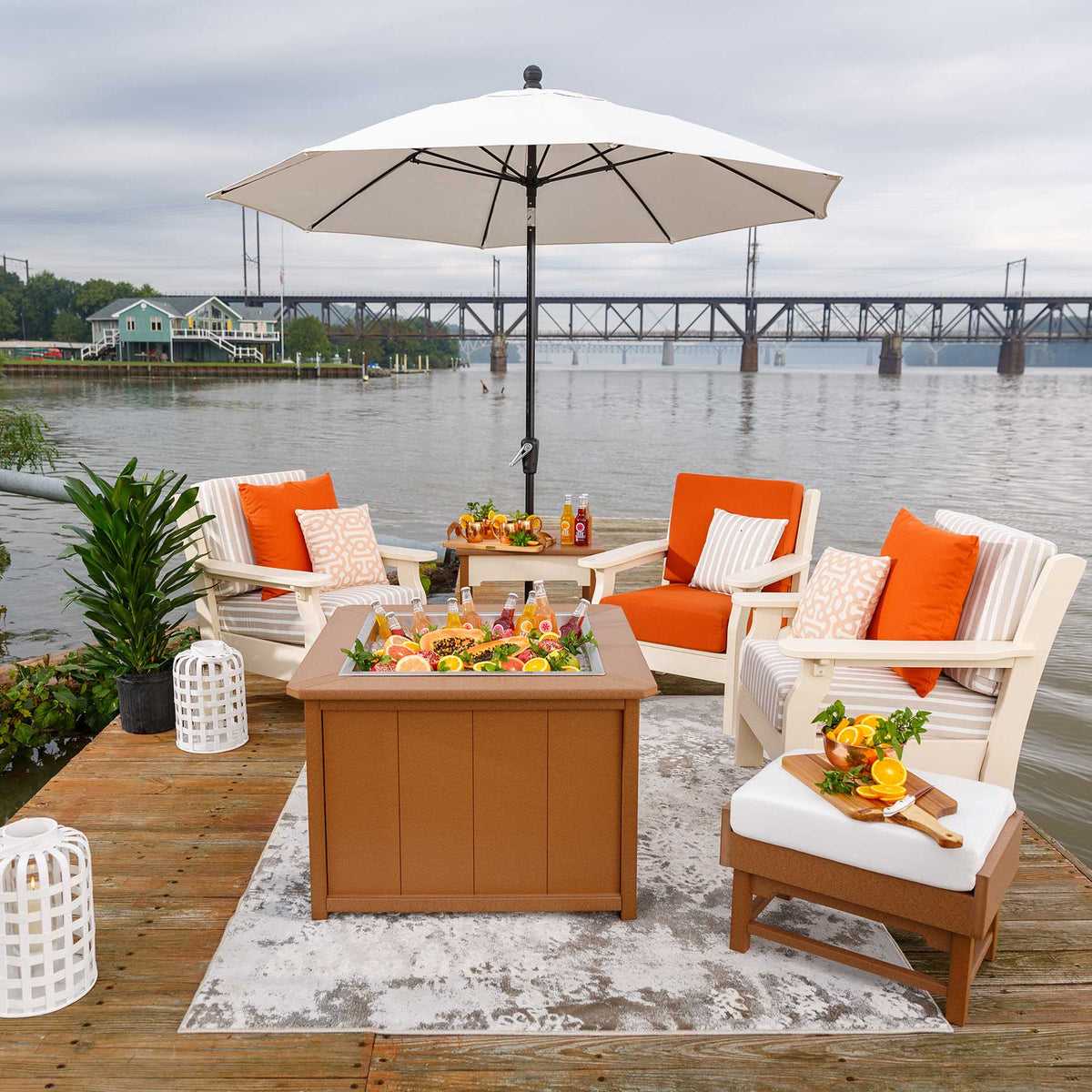 Waterfront dock lounge with a cedar poly ice bucket table full of drinks, four white patio chairs and a market umbrella