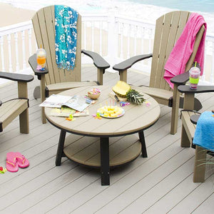 Round weathered wood and black poly patio coffee table with lower shelf, surrounded by Adirondack chairs on a beach deck