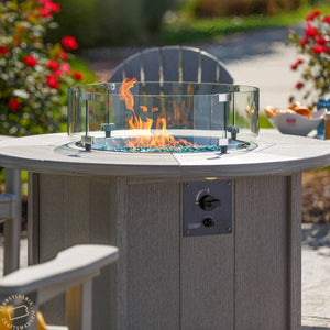 Close-up of flames over blue fire glass inside the glass wind guard of a gray poly round propane fire pit table