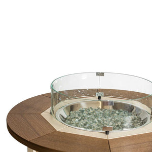 Close-up of a round fire pit table's stainless steel burner bowl filled with clear fire glass under a glass wind guard