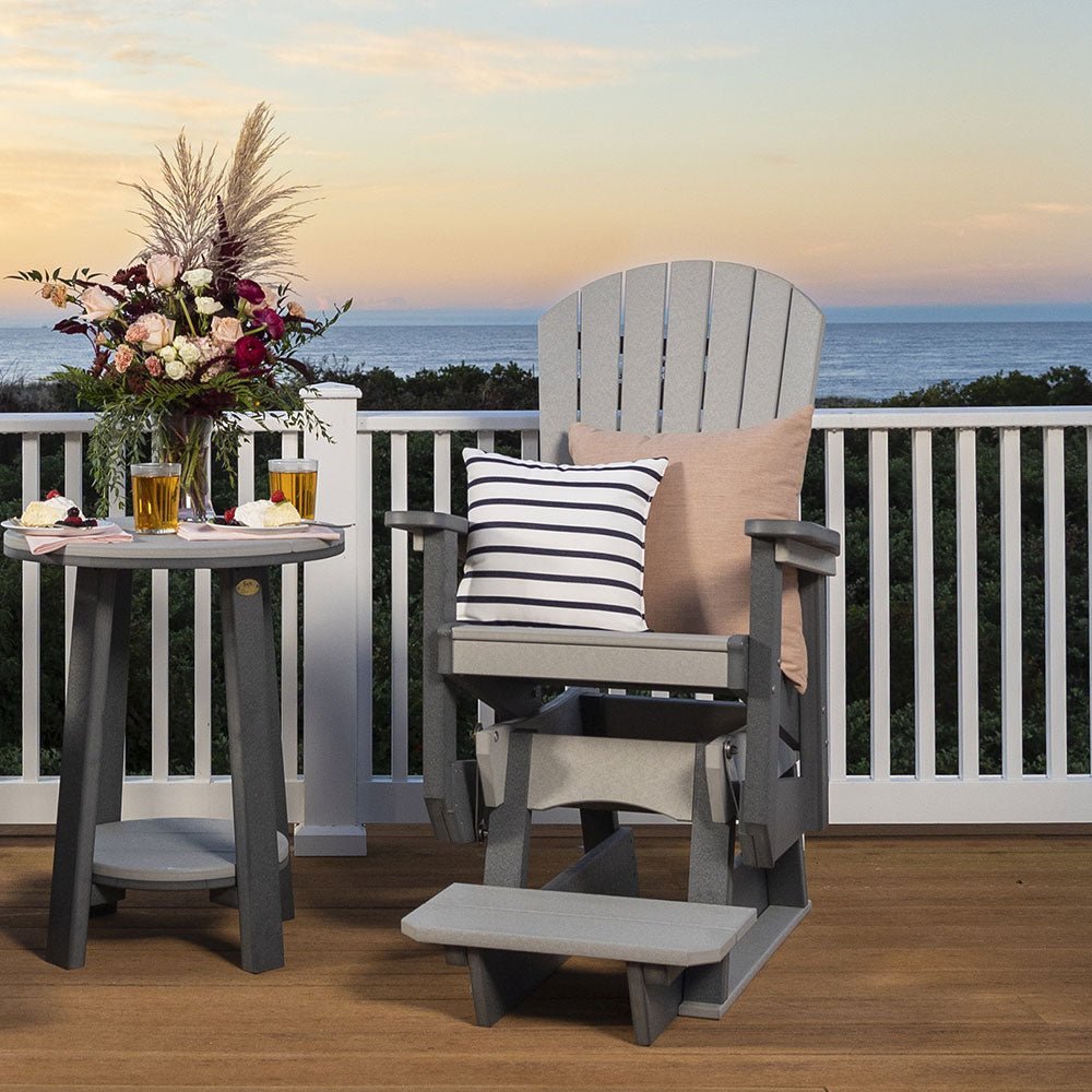 Gray poly counter height Adirondack swivel glider with footrest and striped pillow beside a bistro table at sunset
