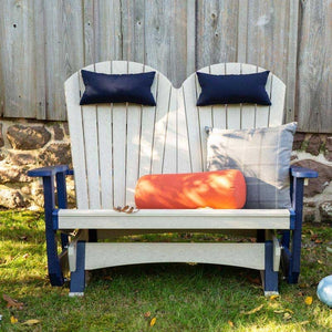 Front view of the birch and navy poly double glider with plush navy, plaid and orange bolster pillows on a lawn