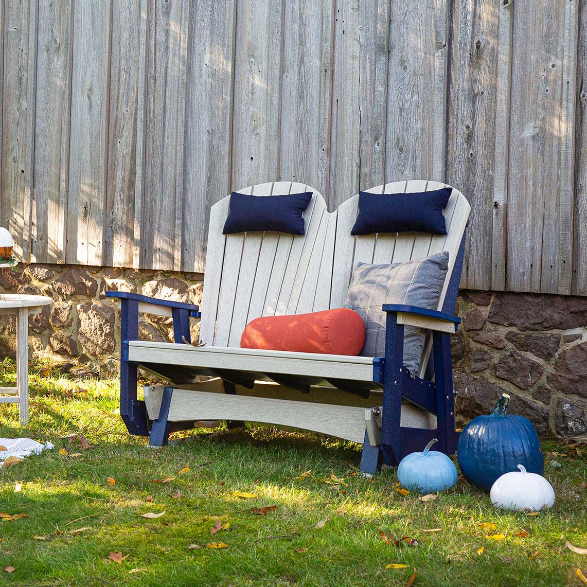 White poly Adirondack outdoor glider bench for two on a stone patio, styled with green and striped pillows