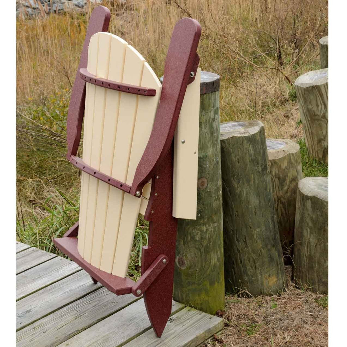 Ivory and cherry folding poly Adirondack chair shown folded upright and leaning against a piling by a boardwalk