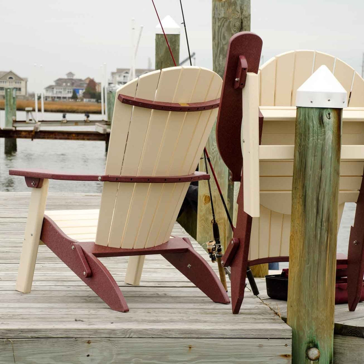 Ivory and cherry folding Adirondack chairs on a marina dock, one open and one folded beside fishing rods