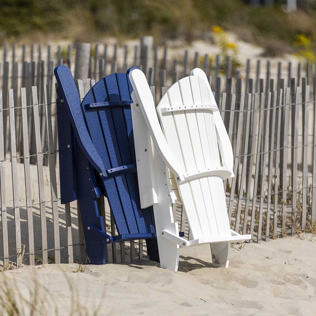 Navy and white folding poly Adirondack chairs shown folded flat and leaning against a beach dune fence