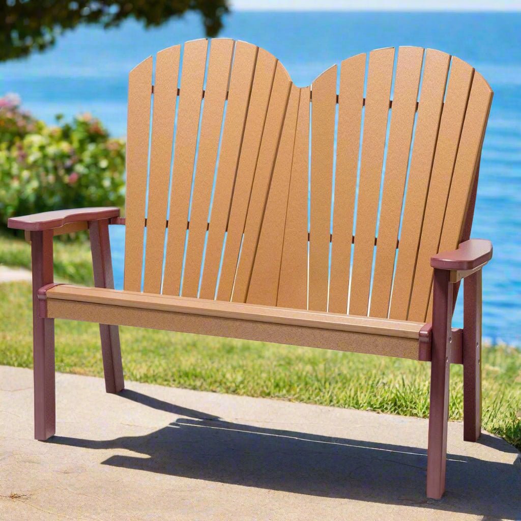 Cedar and cherrywood poly Adirondack bench for two with a double fan back and wide flat arms beside a lake