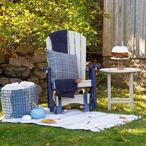 Birchwood and navy poly Adirondack glider chair styled with a plaid pillow, knit throw and pumpkins on a lawn