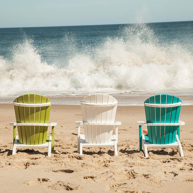 Green, white and teal child Adirondack chairs seen from behind as waves crash on the shoreline