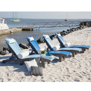 Four blue and gray poly chaise lounges with bolster pillows and a side table on a sandy harbor beach