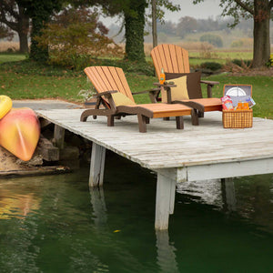 Two cedar and brown poly chaise lounges with a shared table on a lake dock beside kayaks and a picnic basket