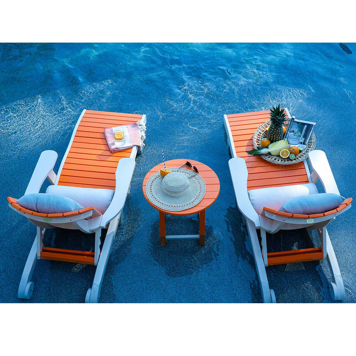 Overhead view of two orange and white poly chaise lounges flanking a round side table on a pool ledge with fruit