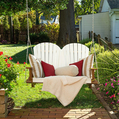 White poly Adirondack porch swing hung on chains with striped and red pillows and a knit throw in a garden