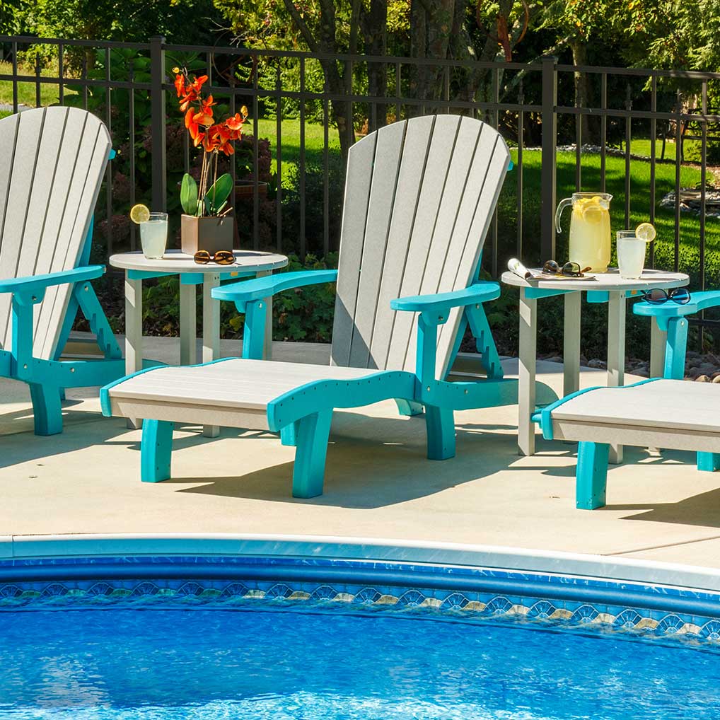 Driftwood and aruba blue Adirondack chairs with ottomans and two round side tables set beside a swimming pool