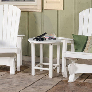 Small round white poly side table holding binoculars and books between two white Adirondack glider chairs