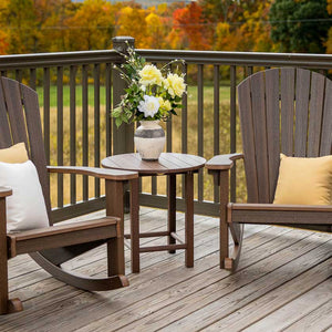 Round brown poly side table with flowers between two matching Adirondack rockers on an autumn deck