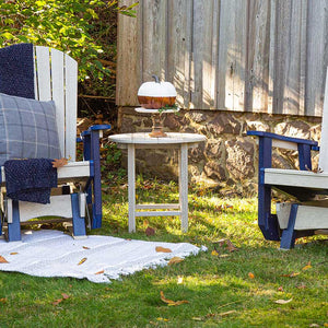 Birchwood poly round side table holding a decorative pumpkin between two navy and cream gliders on a lawn