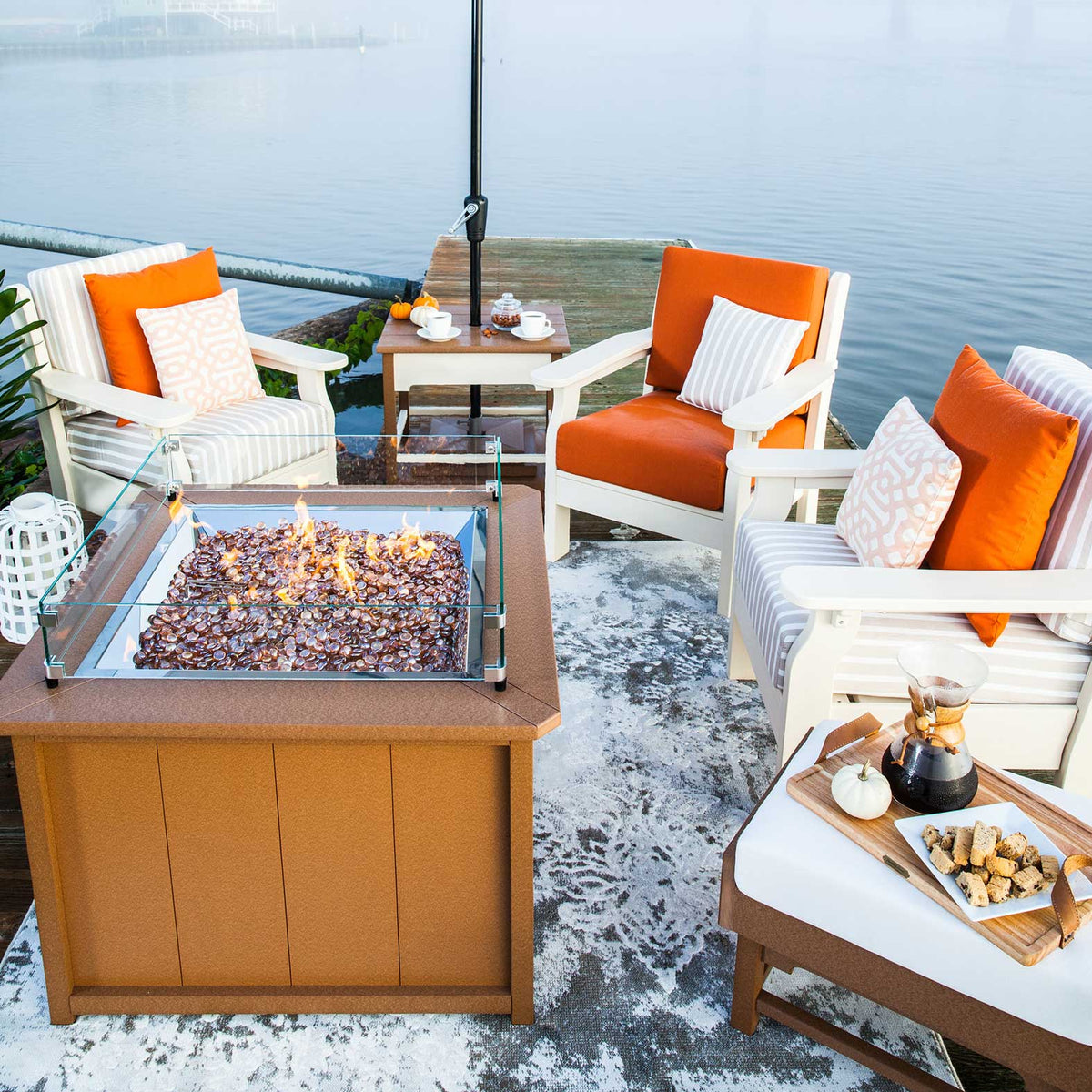 Cedar square poly fire pit table lit on a foggy dock with white deep seating chairs and orange pillows