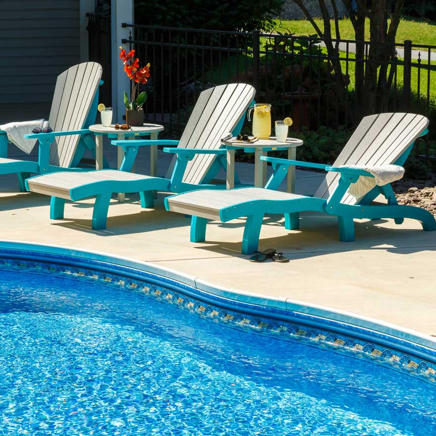 Poolside grouping of aruba blue and driftwood chaise lounges with lemonade and flowers on round side tables