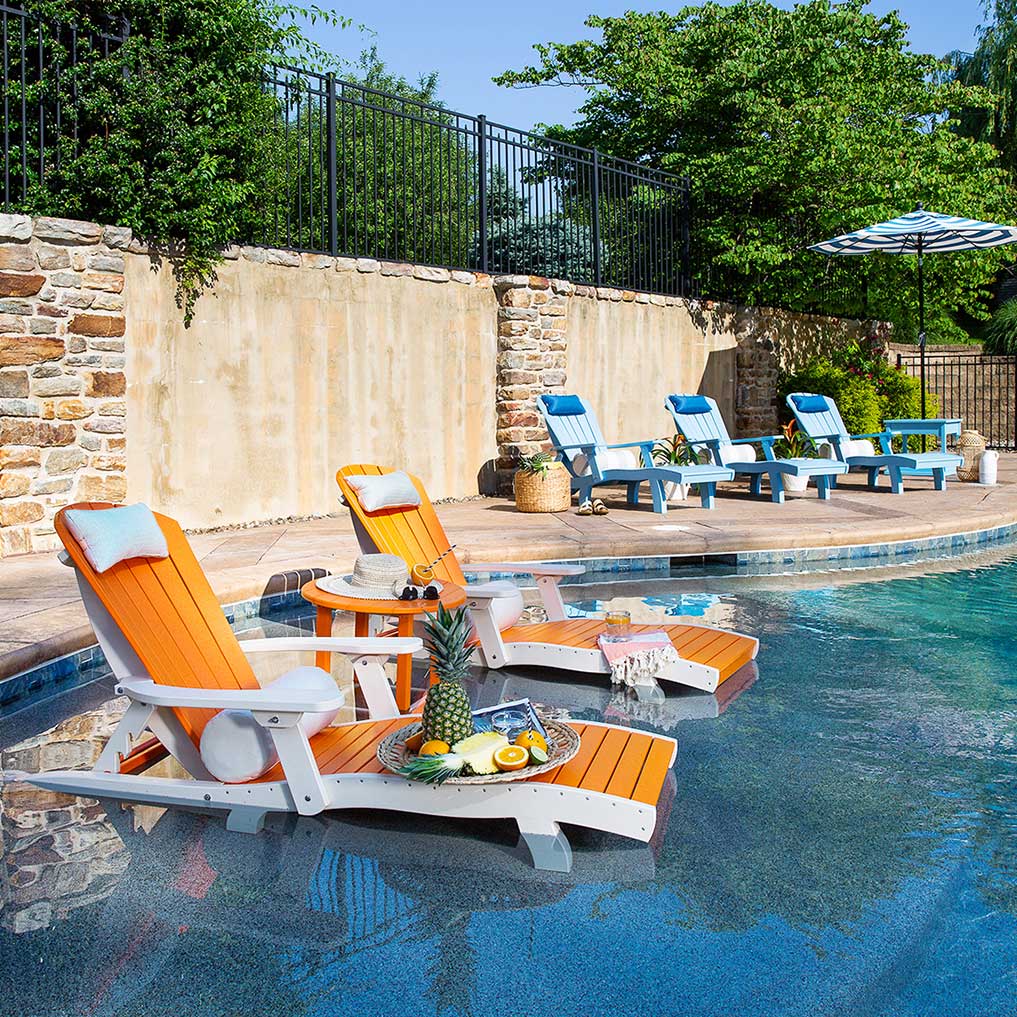 Orange and white poly chaise lounges with a round table of fruit set in the shallow ledge of a stone pool