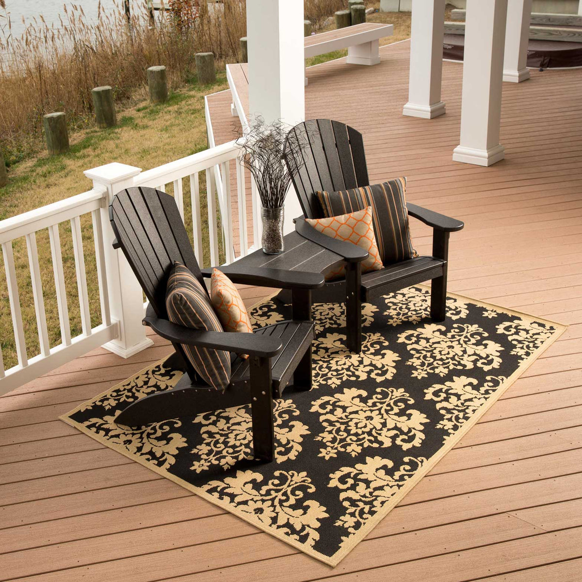 Two black poly Adirondack chairs joined by a center table attachment with striped pillows on a waterfront porch