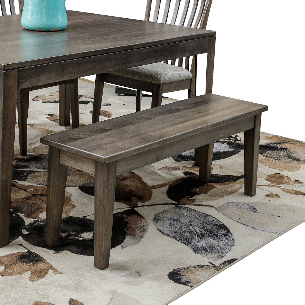 Weathered gray dining bench with a smooth wood seat and tapered legs, on a floral rug beside a matching gray dining table