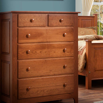 Cherry chest of six drawers photographed in a bedroom beside a panel bed with patterned bedding