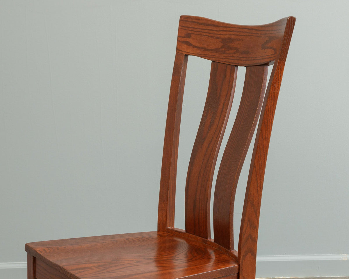 Detail of a chestnut stained oak chair back showing the curved crest rail, wavy slats and grain of the solid seat