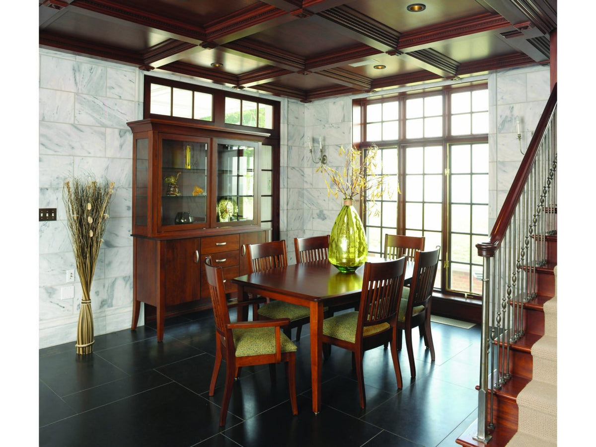Cherry dining table with slat back upholstered chairs and a lighted china cabinet in a marble walled room
