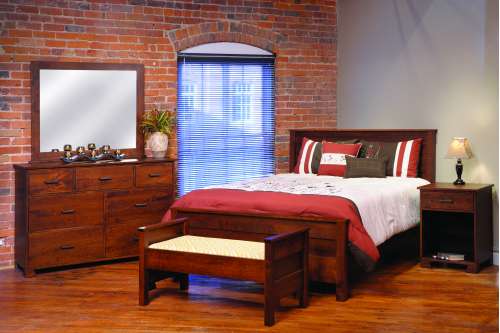 Brick-walled bedroom staged with a cherry panel bed, bench, dresser with mirror and open nightstand