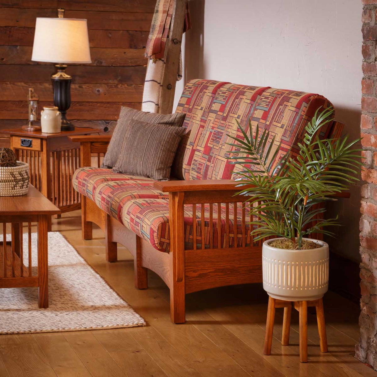 Mission oak sofa in multicolor patchwork fabric beside a lamp table in a room with barnwood and brick walls
