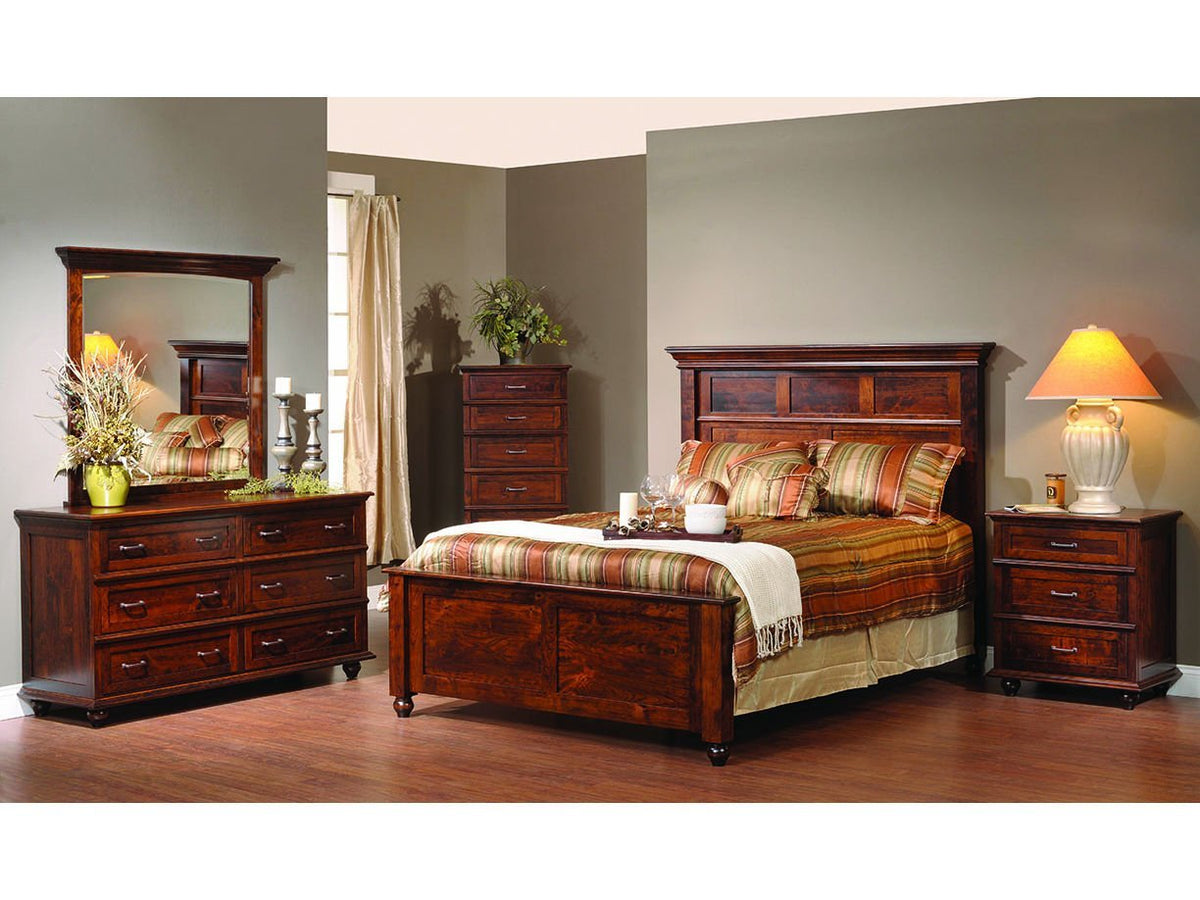 Traditional cherry bedroom set staged with a striped comforter, dresser mirror, tall chest and lamp-lit nightstand