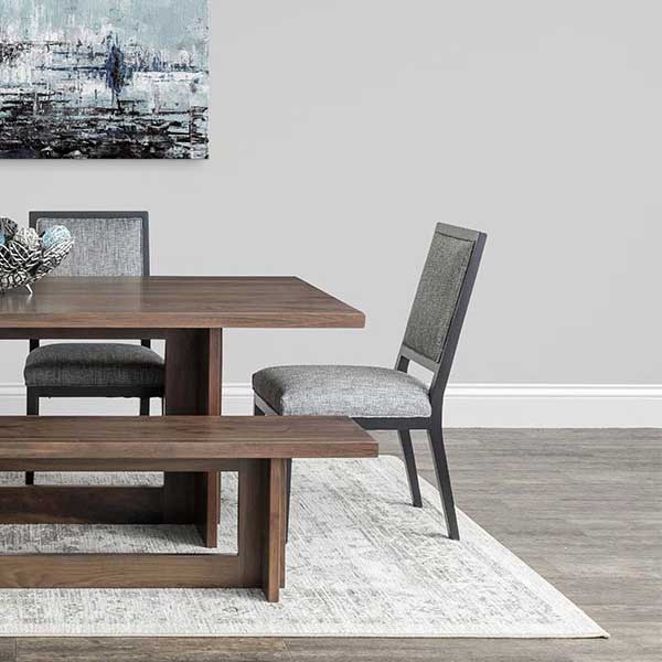 Modern dining chairs with gray woven upholstery and black frames at a walnut table with a matching bench on a pale rug