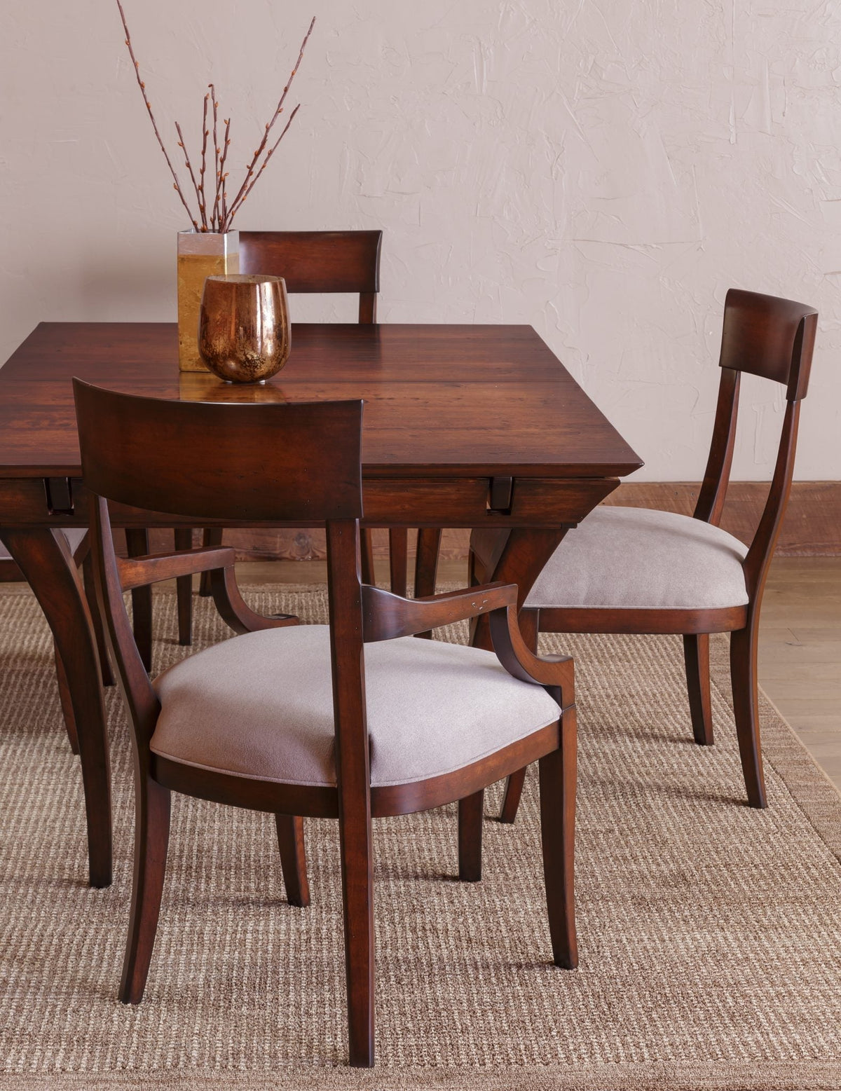 Dark cherry dining table with curved back chairs and cream cushioned seats on a woven rug in a plaster walled room