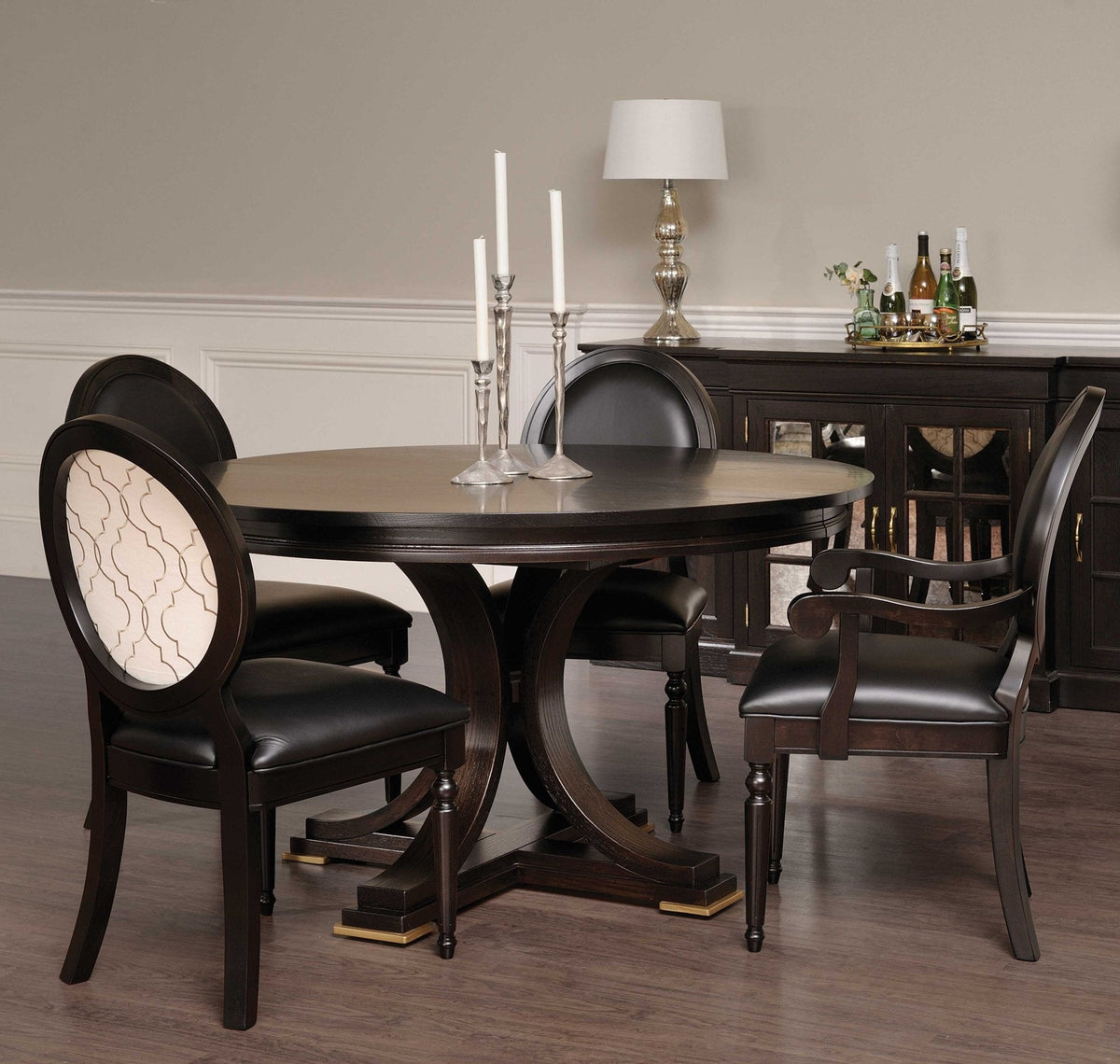 Round pedestal dining table in espresso finish with black leather oval back chairs and a mirrored sideboard behind