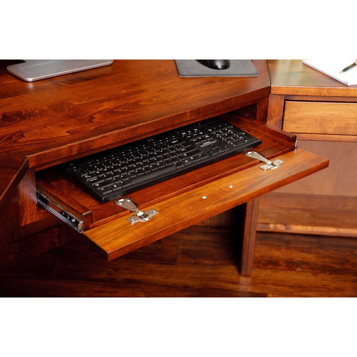 Pull out keyboard tray on a cherry desk holding a black keyboard, with a flip down front panel