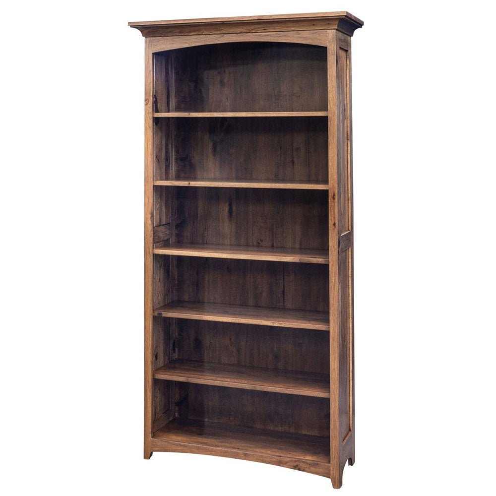 A tall, rustic wooden bookcase with five shelves stands against a light beige wall in a room with hardwood floors. The bookcase is styled with books, a small bird figurine, and a cup on the shelves.