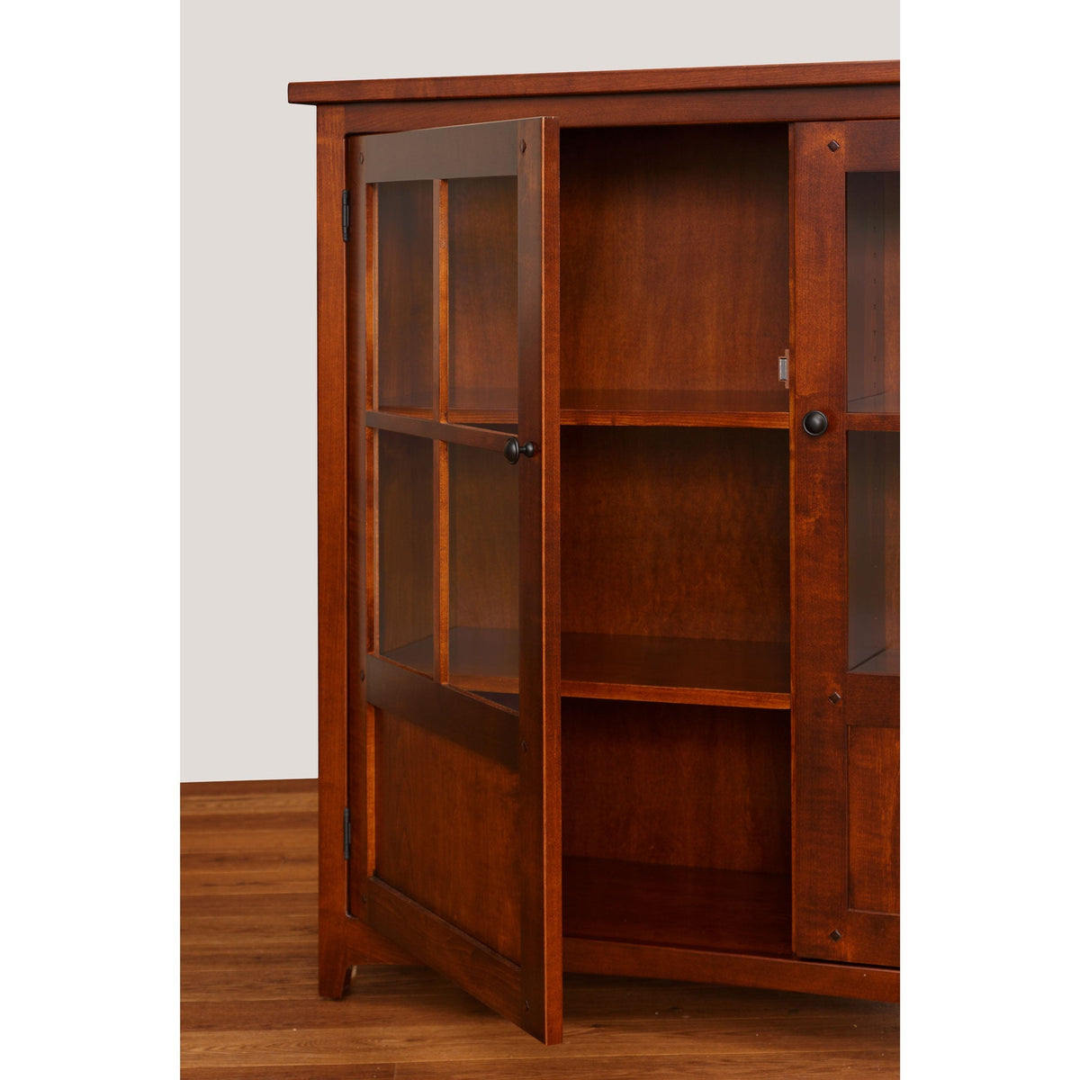 Cherry bookcase with one glass door swung open showing adjustable interior shelves and a paneled lower panel