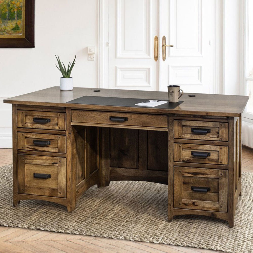 Executive desk in rustic hickory with seven drawers, black handles and a leather desk pad, styled on a woven rug