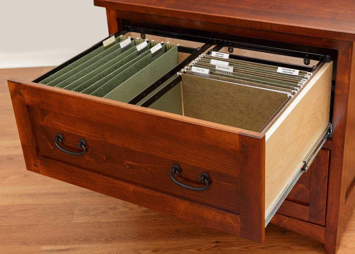 Open lateral file drawer with dovetailed sides holding labeled green hanging folders in a cherry cabinet