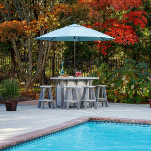 Two-tone gray poly patio bar island with four saddle stools and a blue umbrella beside a swimming pool