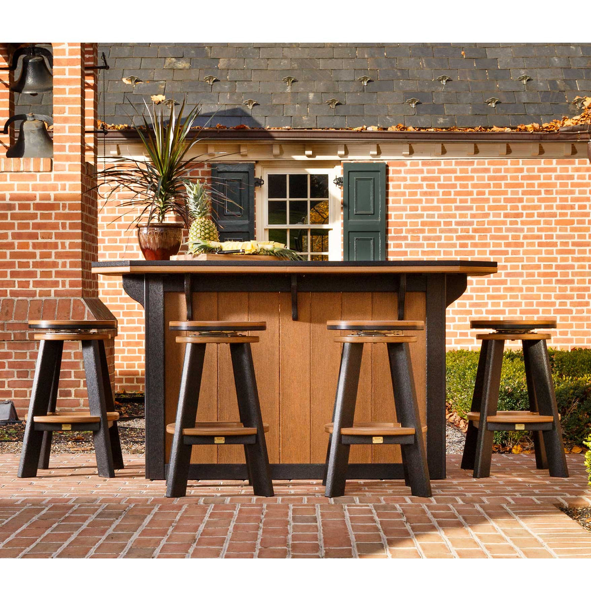 Cedar and black poly bar island with four backless swivel bar stools set against a brick colonial house