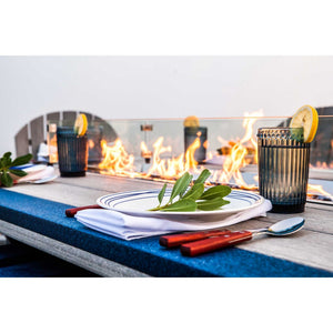 Place setting with lemon garnished glasses beside a lit fire trough on a gray and blue poly fire table