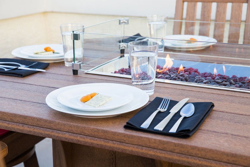 Dinner setting beside the glass-enclosed flame trough of a warm brown poly outdoor dining table