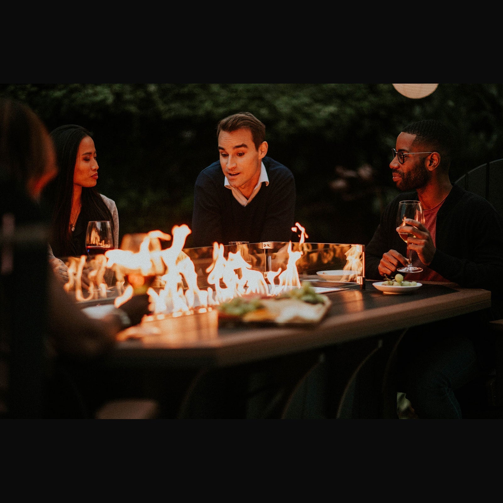 Driftwood and navy poly fire pit dining table with six Adirondack dining chairs on a rug at a misty dock